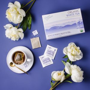 image of box and a brewed cup of Prince of Peace White tea, with white flower in a blue background